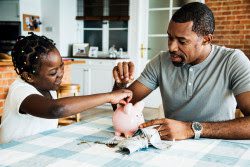 Father and daughter putting money into a piggy bank.