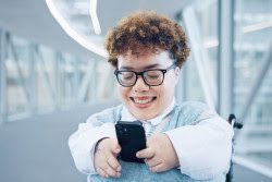 A person with a disability looking at a cell phone and smiling.