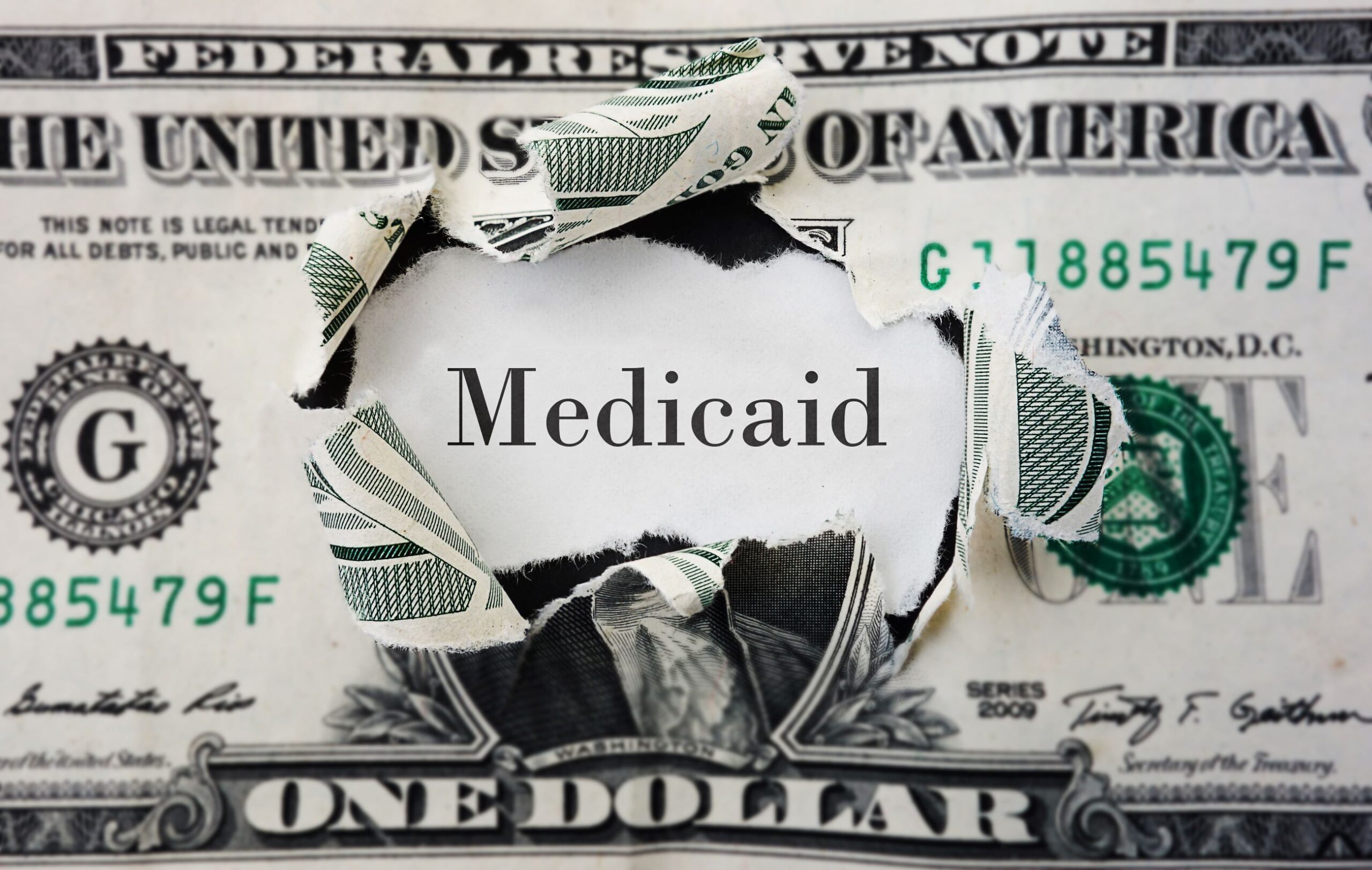 A dollar ripped in the center with the word "medicaid" showing through.